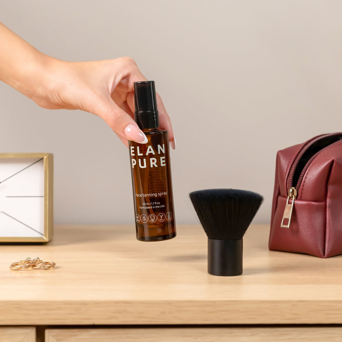 Hand holding an 'ELAN PURE' bottle on a wooden surface with a brush and bag in the background.