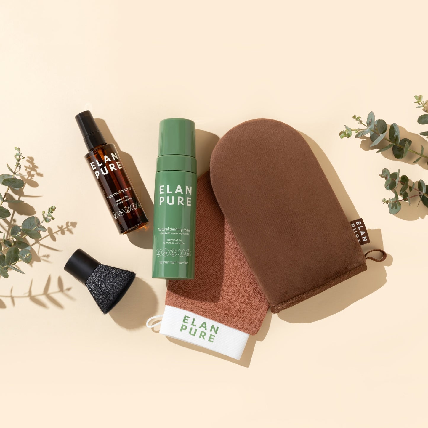 Elan Pure skincare products including a Self-Tan, Face Tanning Mist, Brush, Exfoliating Mitt, and Tanning Mitt on a beige background with eucalyptus leaves.