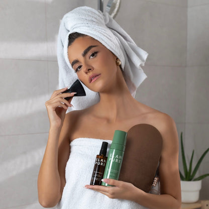 Woman holding the Elan Pure Face Tanning Mist, Self-Tan, Tanning Mitt and brush in the bathroom.