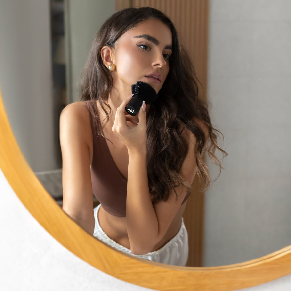Woman applying Face Tanning Mist with the Elan Pure Brush in front of a mirror with a wooden frame.