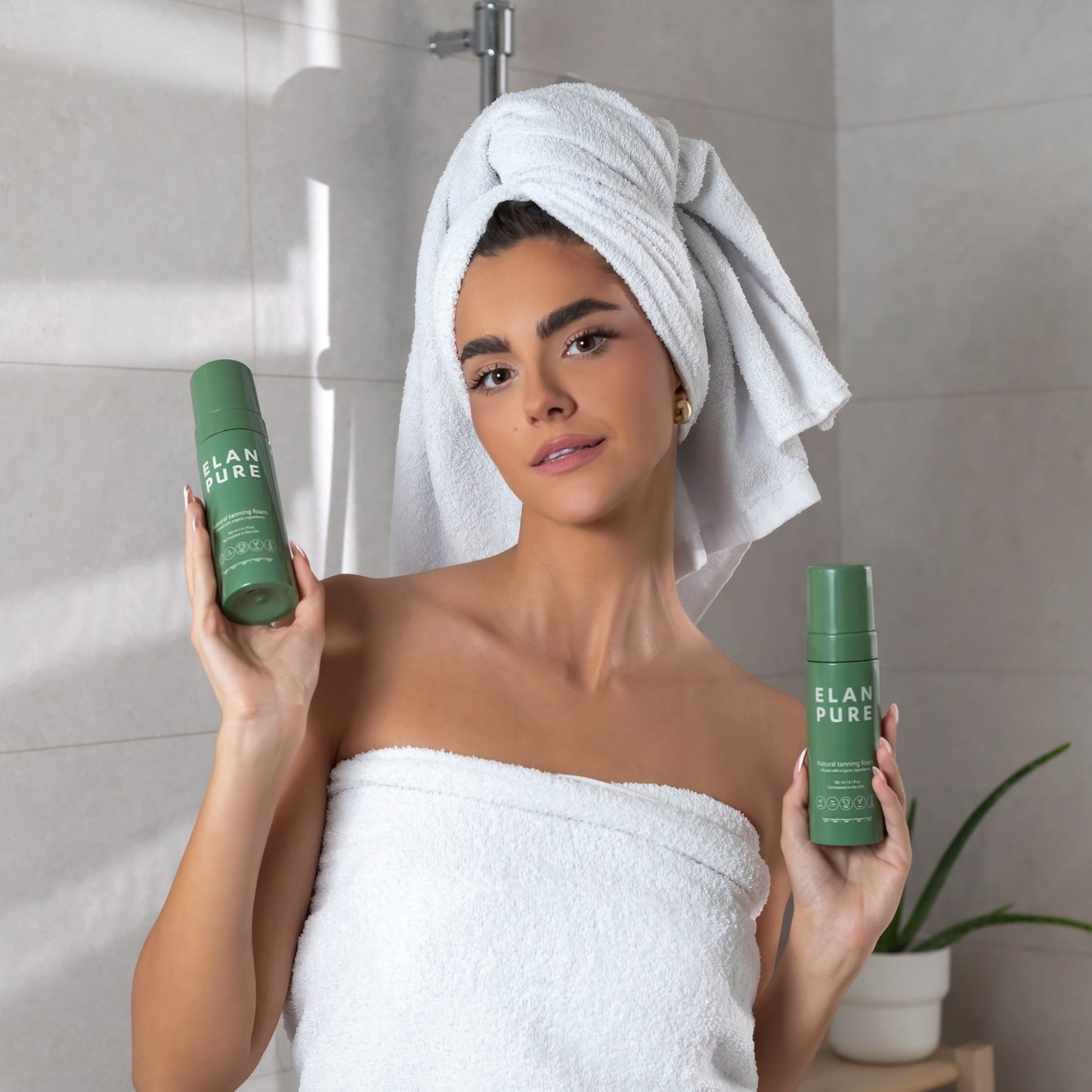 Woman holding up two Elan Pure Self-Tan bottles in a towel in the bathroom.