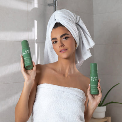 Woman holding up two Elan Pure Self-Tan bottles in a towel in the bathroom.