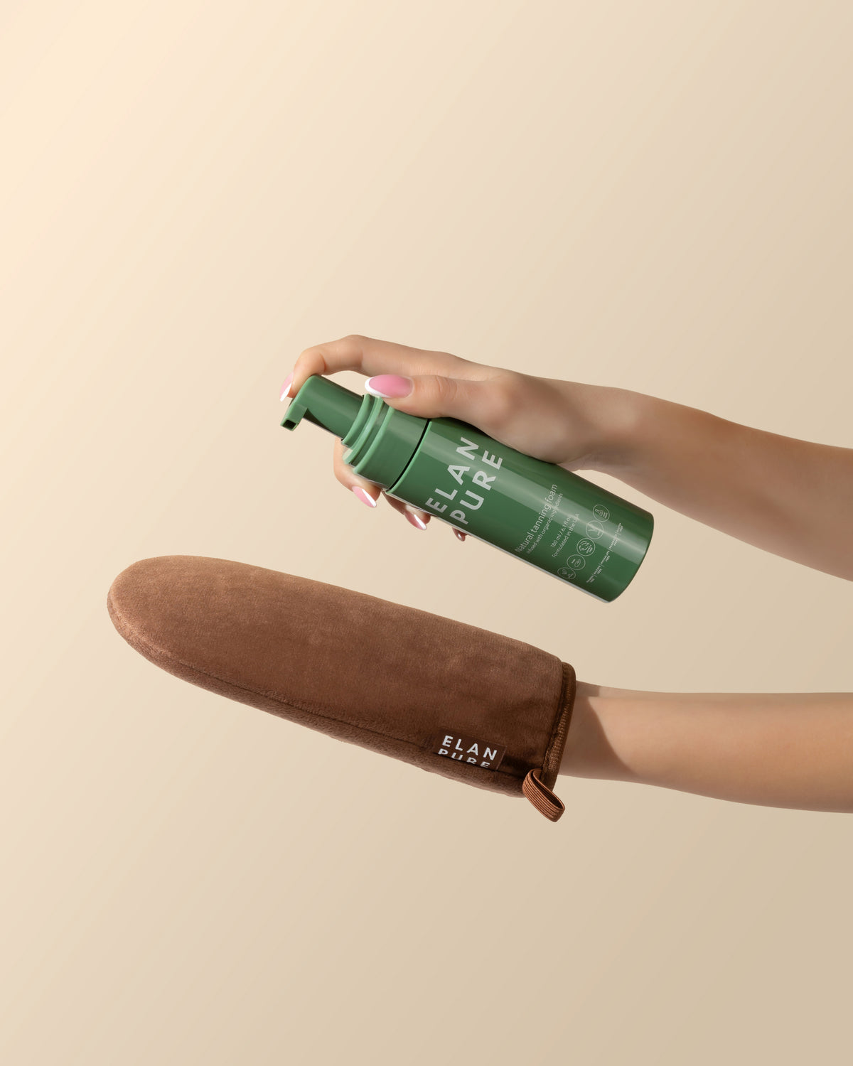 Hand holding Elan Pure self-tan over the tanning mitt against a beige background.