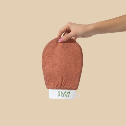 Hand holding the Elan Pure Exfoliating Mitt on a beige background.